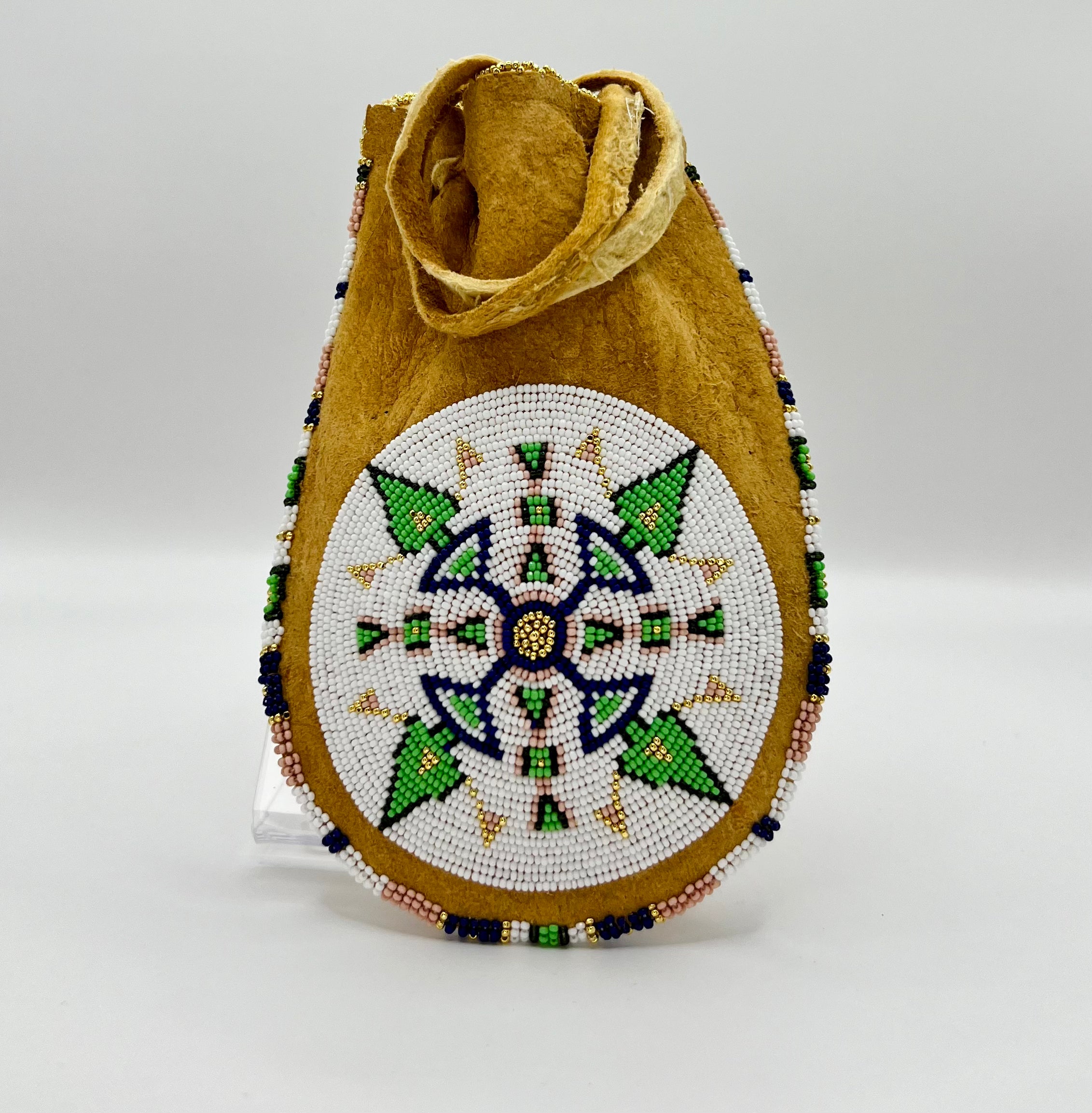 A beaded bag with geometric patterns predominantly in white, green, and purple colors, with a tan background.